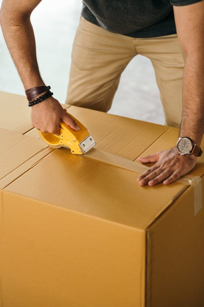 Unrecognizable man sealing box with duck tape while preparing for moving out